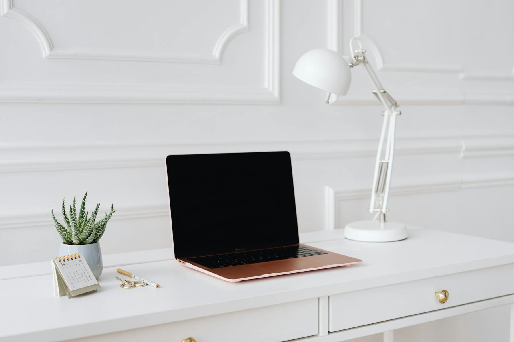 A clean and elegant workspace featuring a laptop, desk lamp, and plant on a white desk. on The Digital Hustler