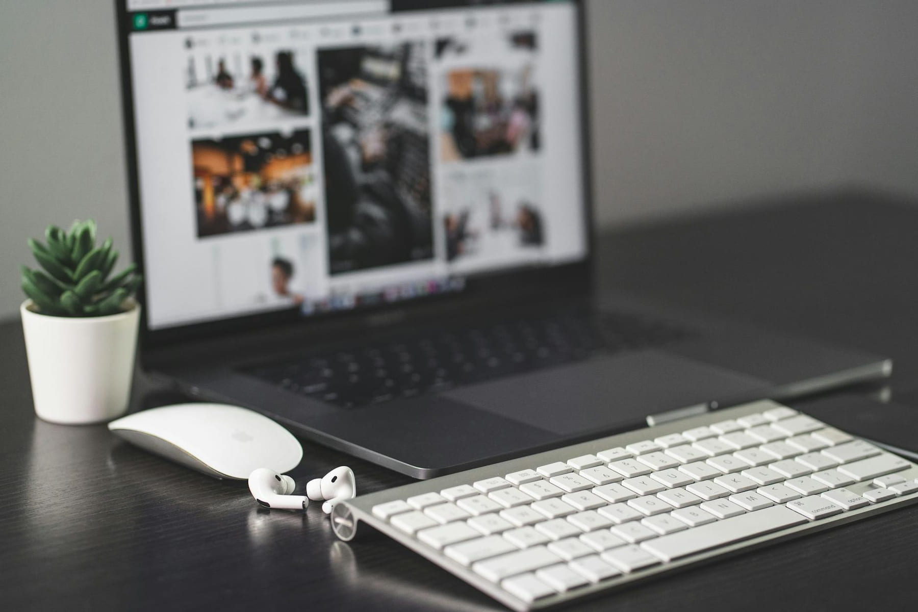 A sleek modern workspace featuring a laptop, keyboard, mouse, AirPods, and a small plant. on The Digital Hustler