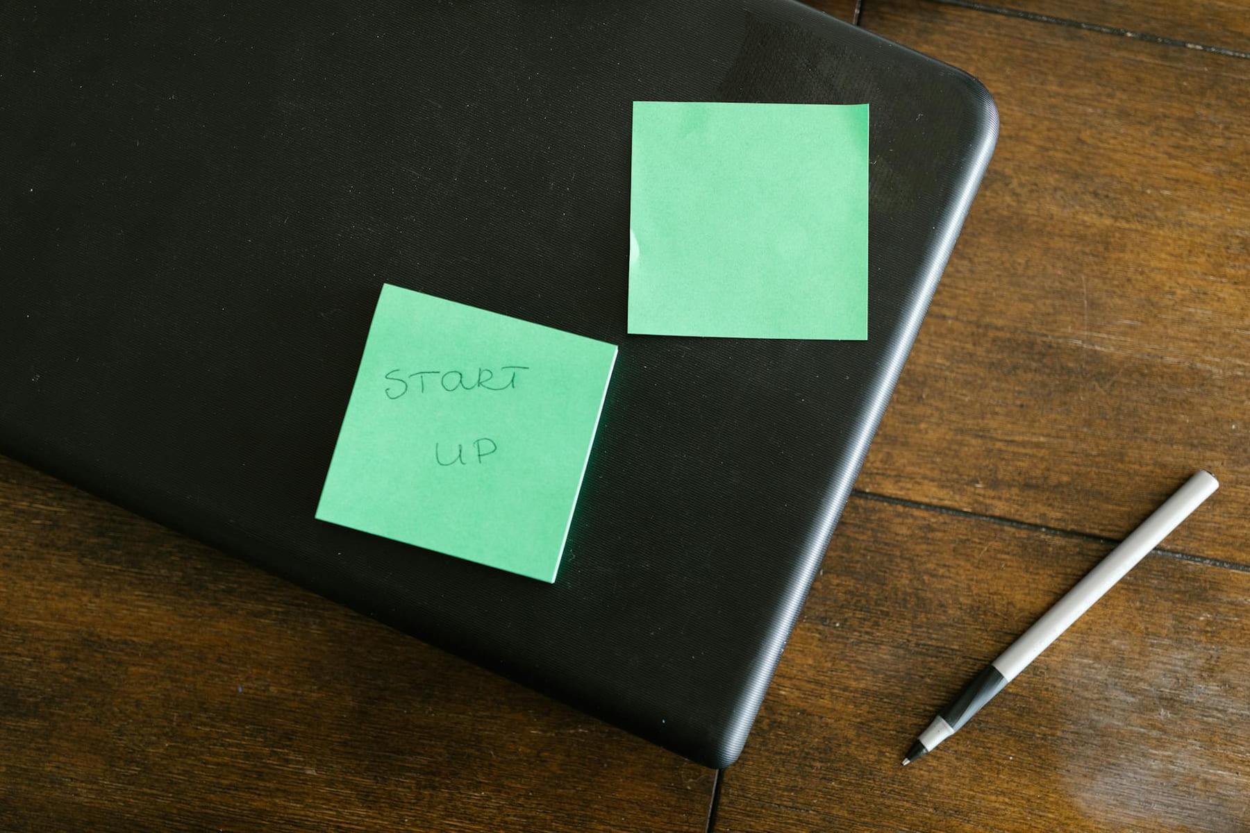 A laptop with green sticky notes and a pen on a wooden desk, symbolizing startup planning. on The Digital Hustler