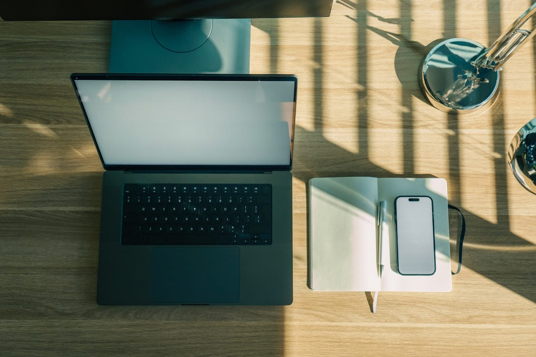 Laptop, phone, and notebook on a wooden desk. on The Digital Hustler