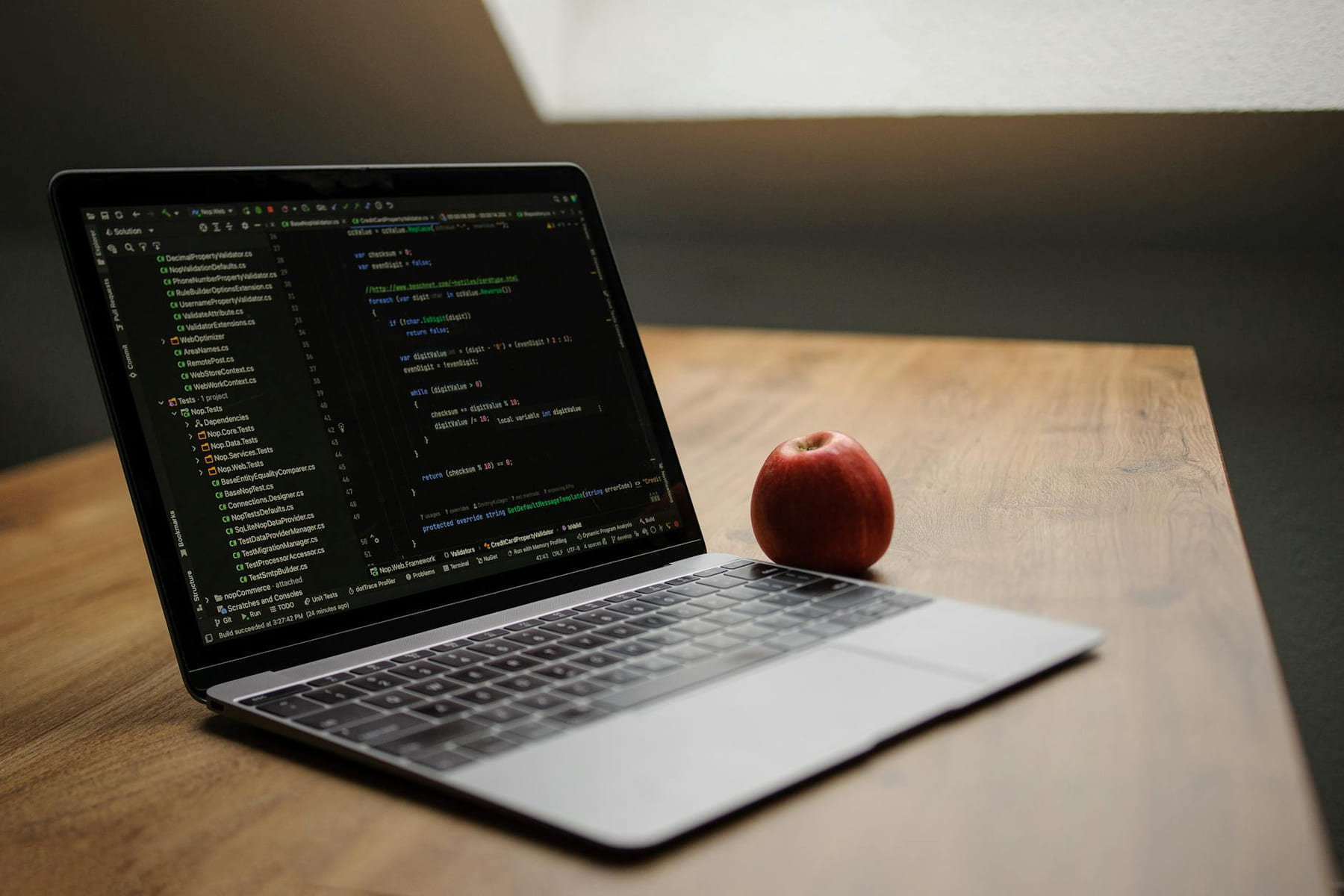 Open laptop displaying code next to a red apple on a wooden desk. on The Digital Hustler