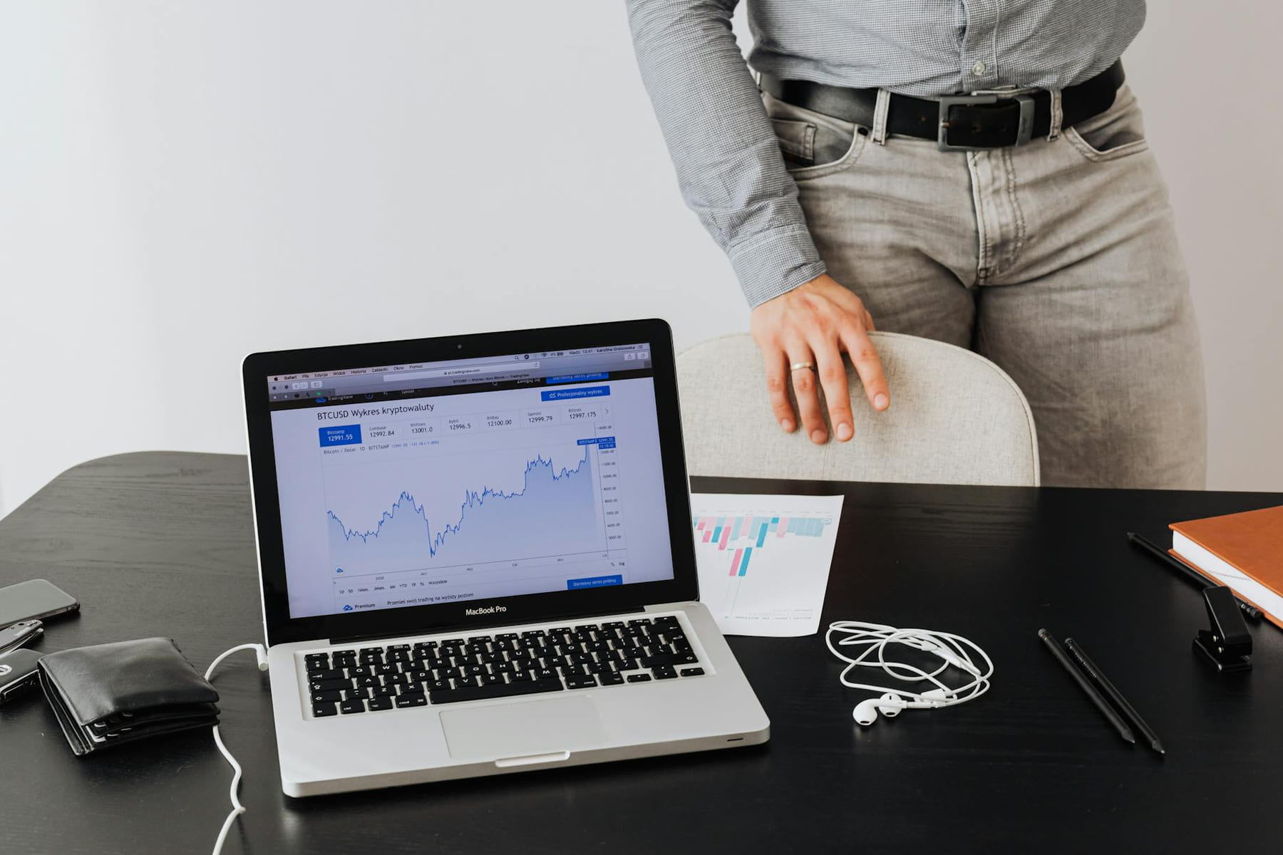A businessman stands next to a laptop displaying cryptocurrency data, symbolizing modern digital finance. on The Digital Hustler