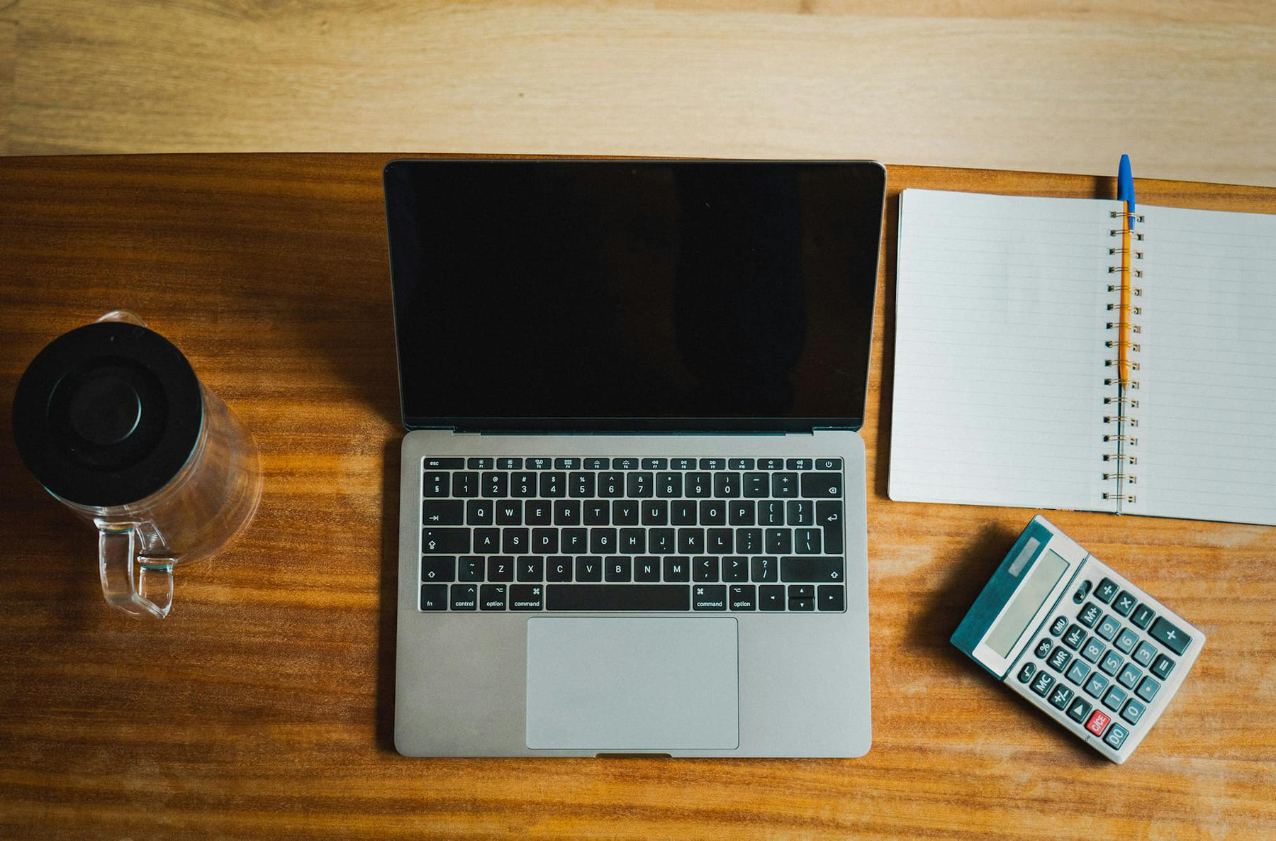 Flat lay of workspace featuring a laptop, calculator, and notebook on a wooden desk. on The Digital Hustler