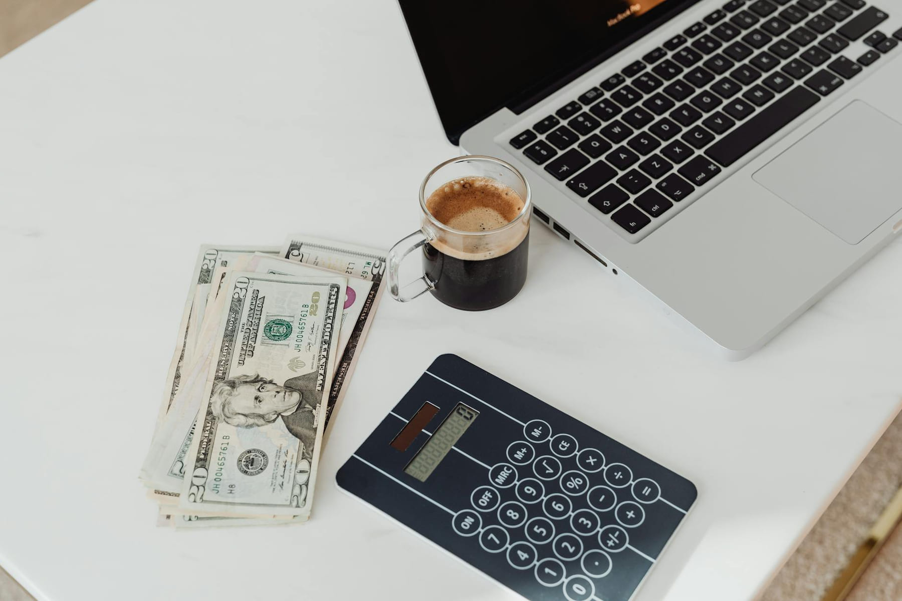 A modern workspace featuring a calculator, cash, and laptop with coffee. on The Digital Hustler