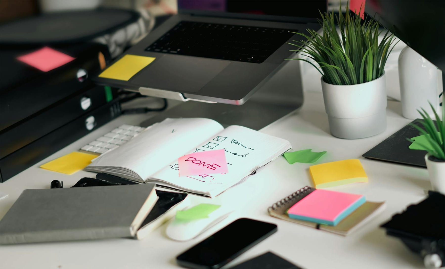 A cluttered office desk featuring a laptop, notebooks, and checklists amid colorful sticky notes. on The Digital Hustler