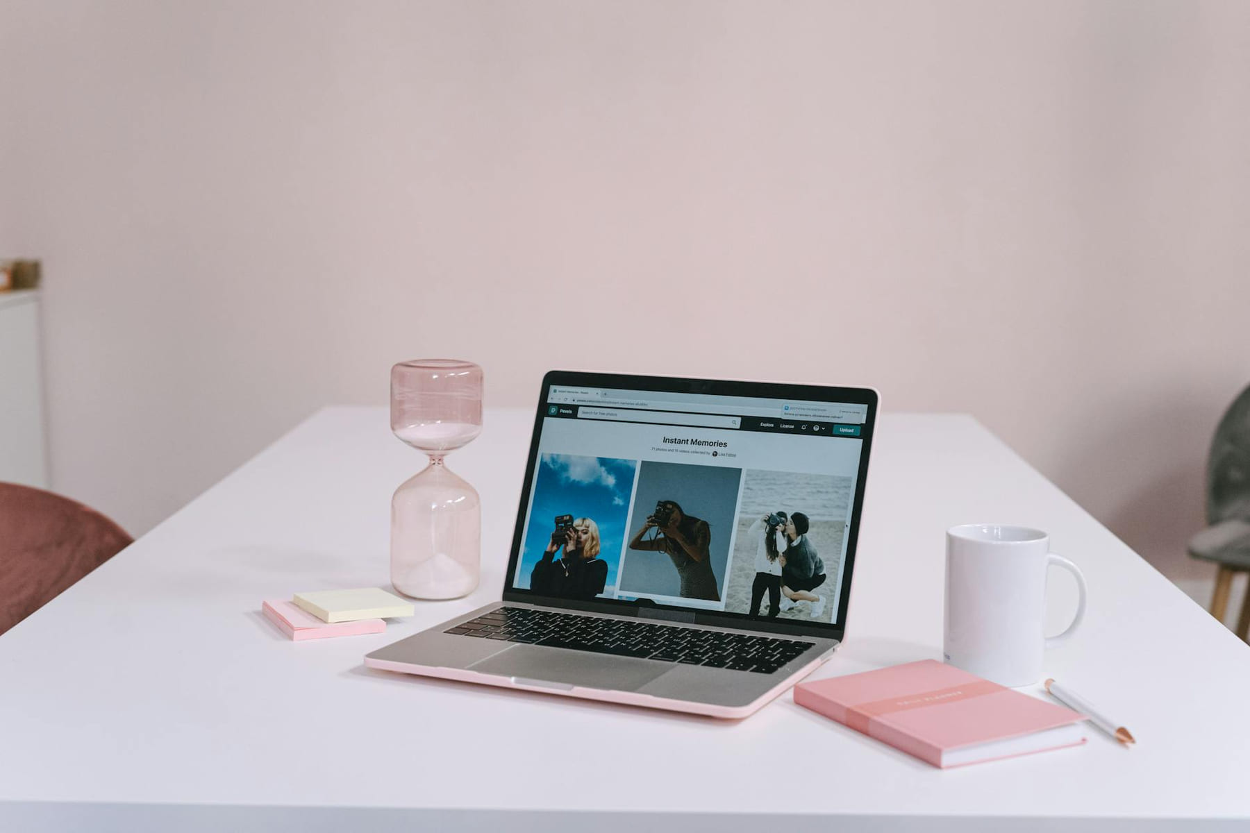 A clean and minimalist workspace featuring a laptop, hourglass, notebook, and coffee mug on a white desk. on The Digital Hustler