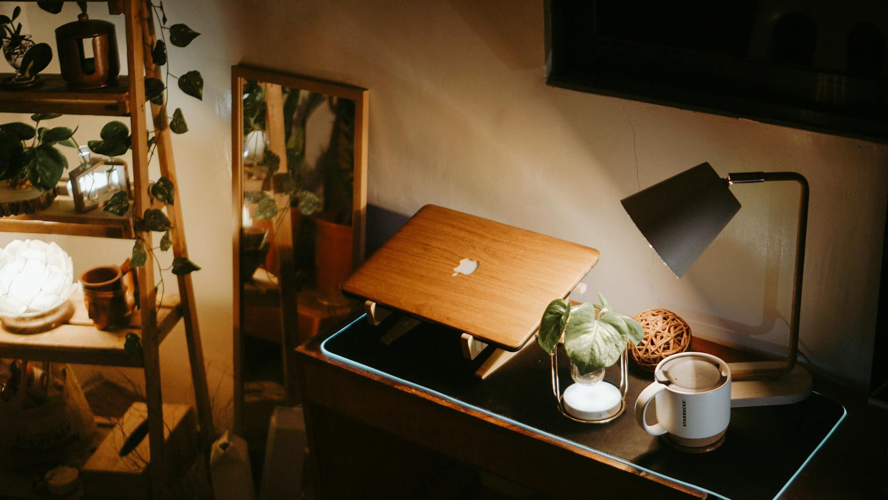 Warmly lit home workspace featuring a laptop, lamp, and green plants on a desk. on The Digital Hustler
