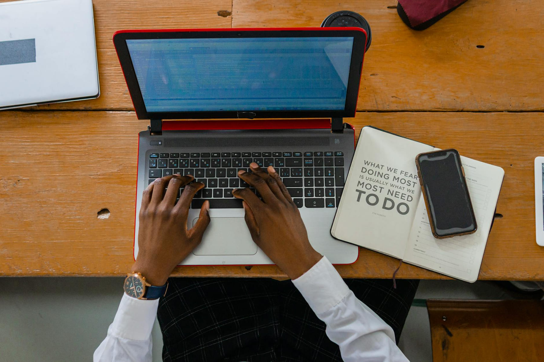 Person typing on a laptop with a notebook and smartphone on a wooden desk. Ideal for business or work themes. on The Digital Hustler