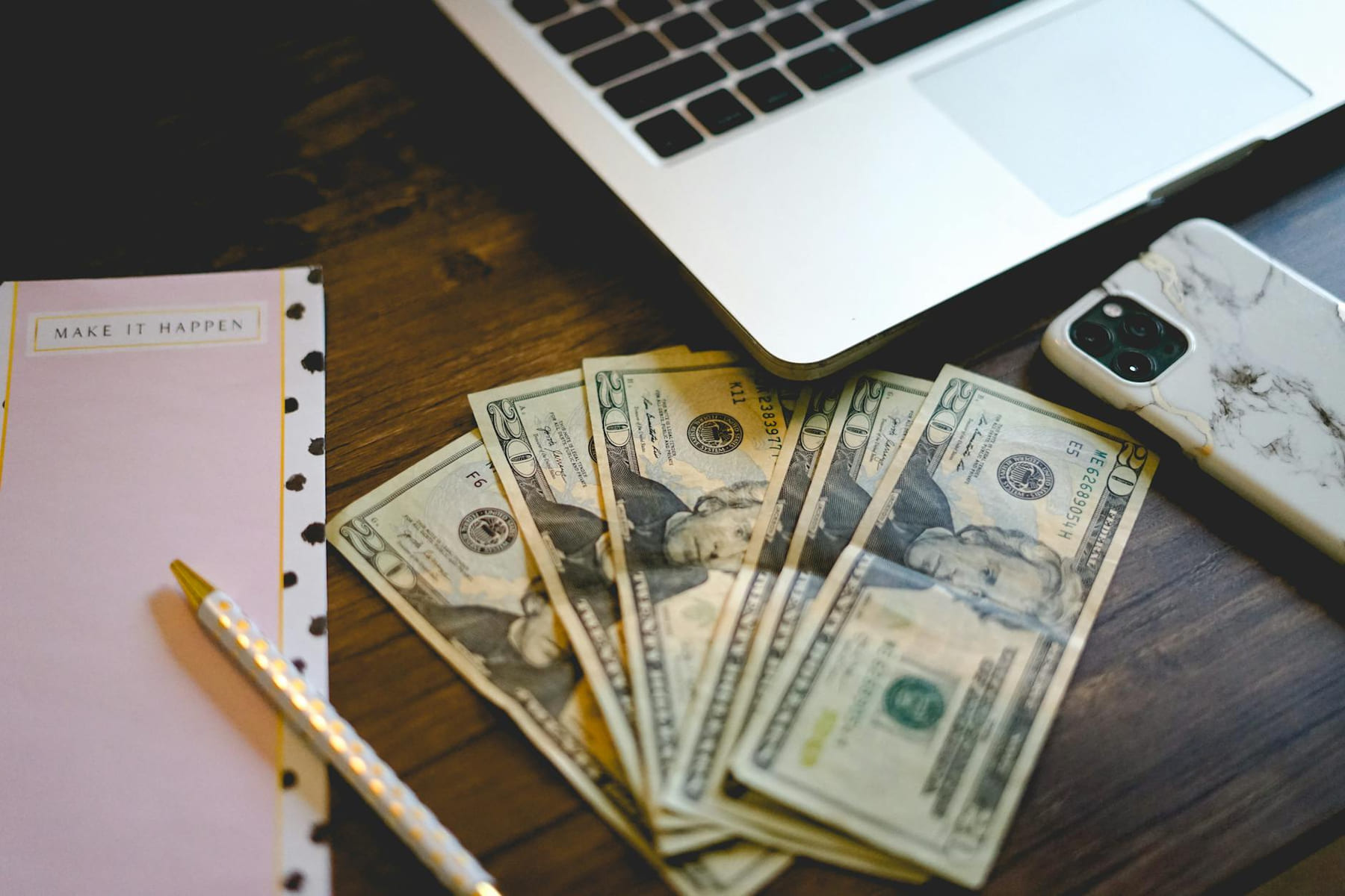 A workspace setup with dollar bills, notepad, and laptop on a wooden desk. on The Digital Hustler