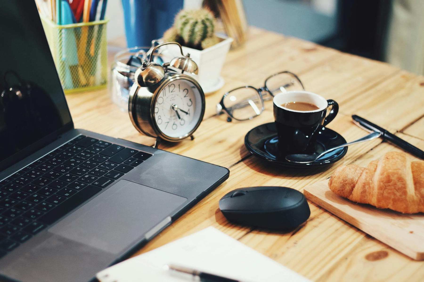 A warm workspace scene featuring a laptop, coffee, croissant, and clock on a wooden desk. on The Digital Hustler